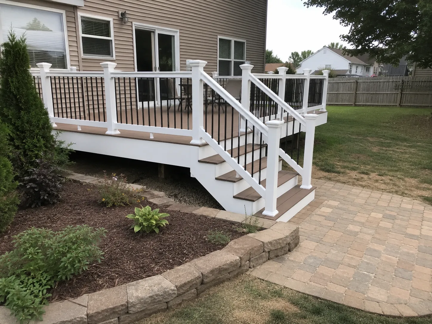 Raised deck with white railing, stairs, and adjacent paver patio
